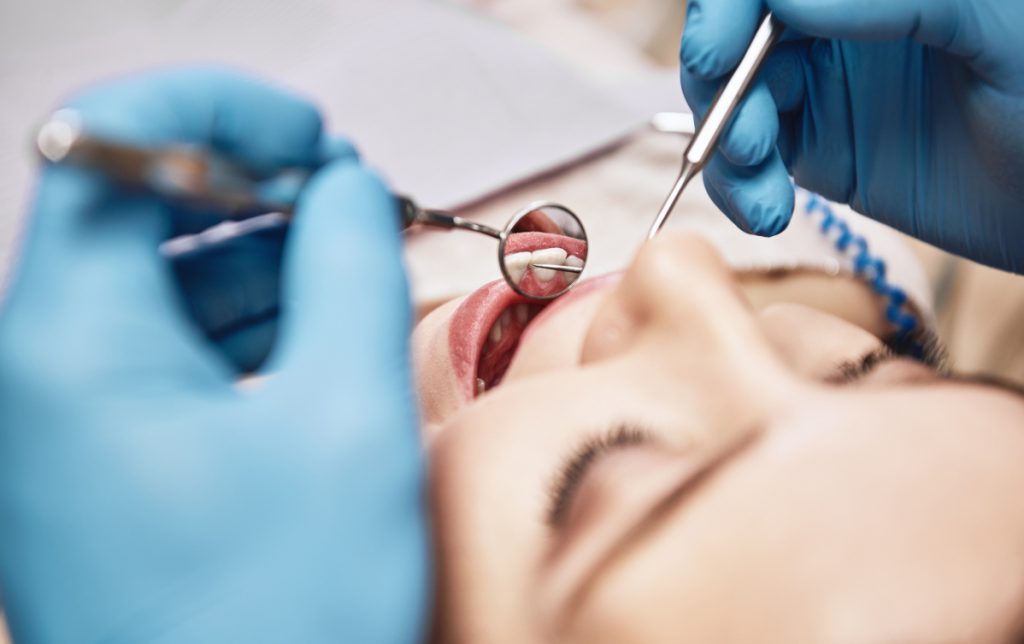 dentist with blue latex gloves holding mirror instrument and cleaning instrument in young girl's mouth for teeth cleaning